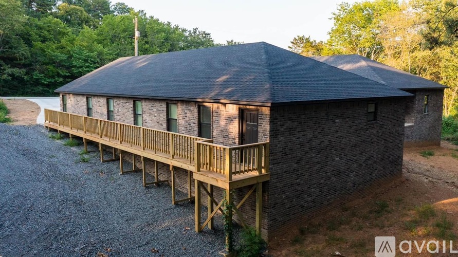 A house with a black roof and wooden deck is surrounded by trees.