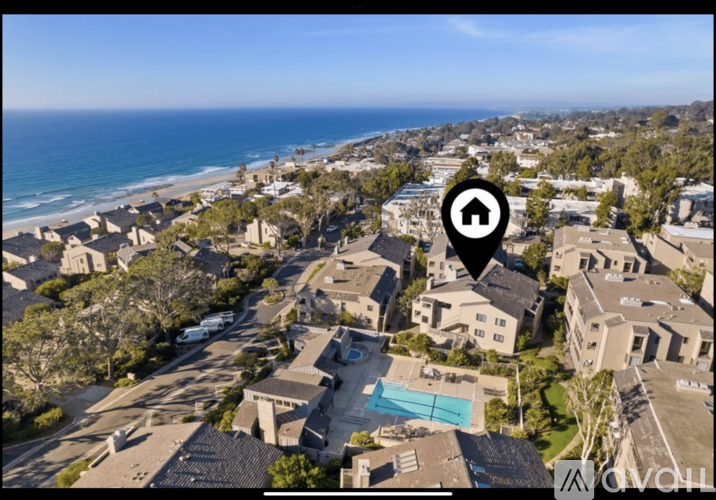 A bird's eye view of a residential area with a swimming pool and a beach in the background.