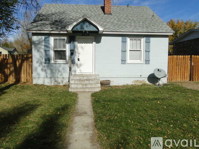 A small blue house with a white door and a satellite dish on the lawn.