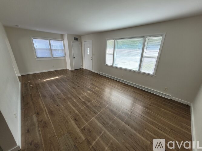A spacious room with wooden flooring and two windows.