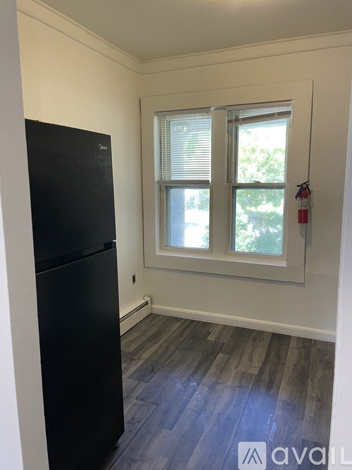 A black fridge in a room with a window and a fire extinguisher.