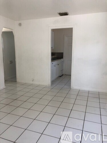 A white tiled kitchen with a doorway leading to another room.