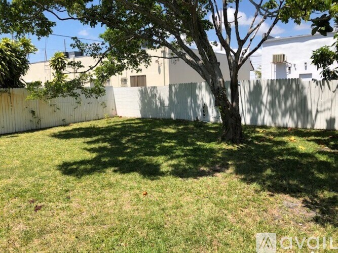 A tree in a yard with a white fence and building in the background.