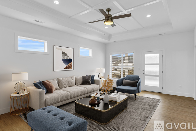 A living room with a grey sofa, a blue ottoman, a coffee table, and a ceiling fan.