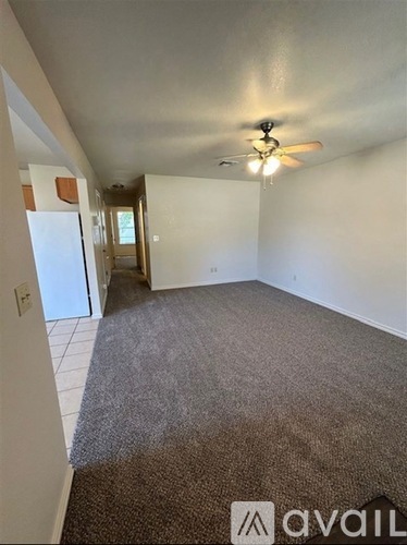 A carpeted room with a ceiling fan and a door leading to another room.