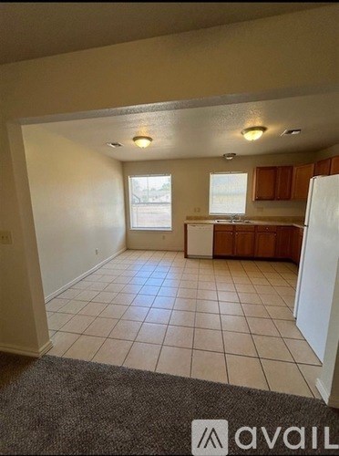 A room with a tiled floor and a kitchen area in the background.