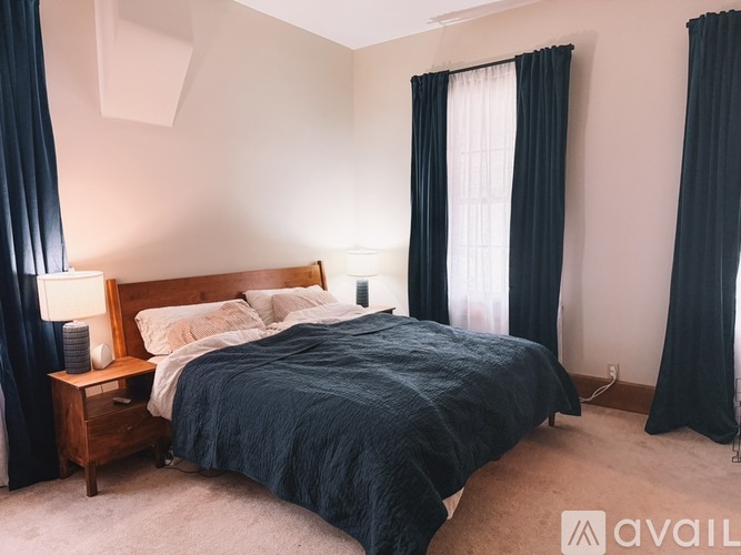A bedroom with a bed, nightstand, and window with curtains.