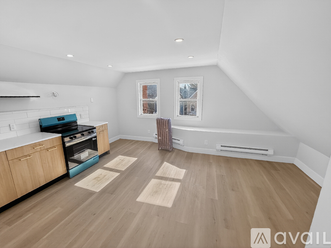 A spacious, empty room with wooden flooring and a kitchen area to the left.