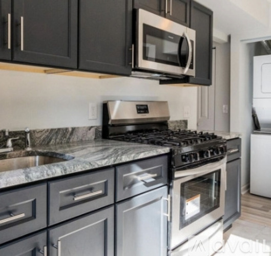 A kitchen with a black microwave above a stove with a marble countertop.
