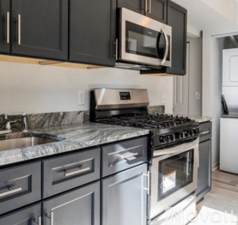 A kitchen with a black microwave above a stove with a marble countertop.
