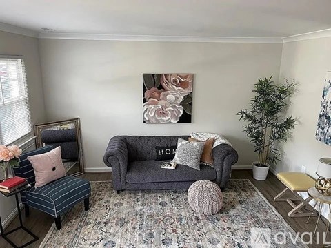 A living room with a grey couch, a small table with a vase of flowers, a chair, and a rug.