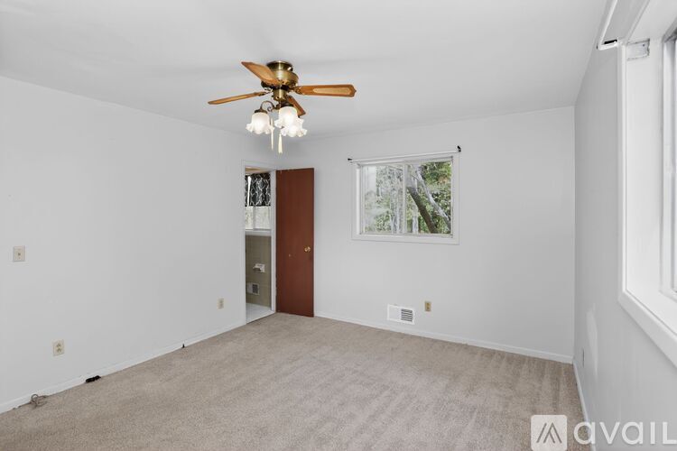 A room with a ceiling fan and a window with a view of trees.