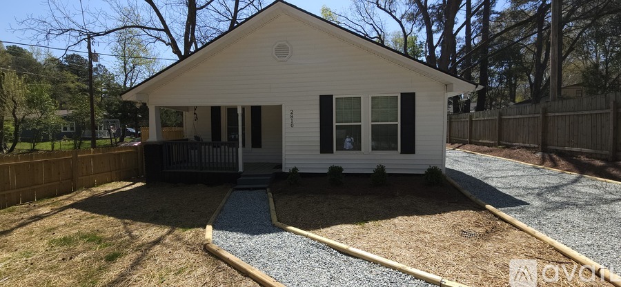 A small white house with a porch and a gravel driveway.