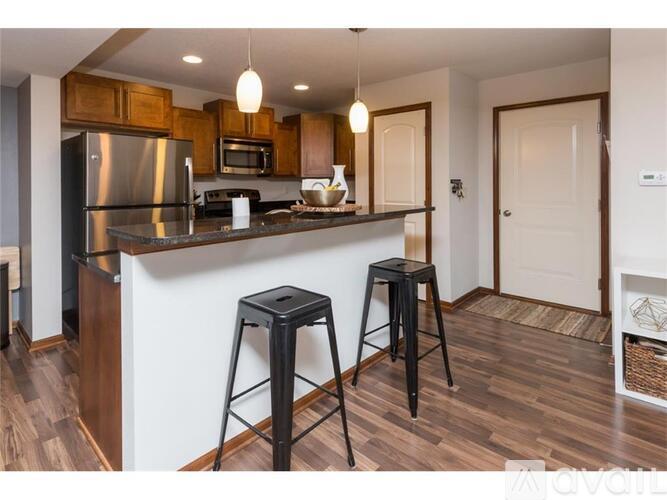 A kitchen with a refrigerator, microwave, and two bar stools.