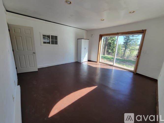 A room with a brown floor and a large window showing trees outside.