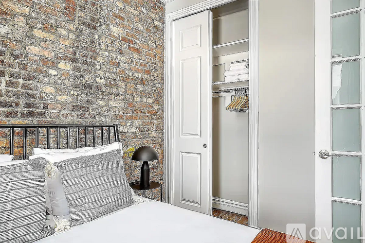 A bedroom with a brick wall and a white door leading to a hallway.