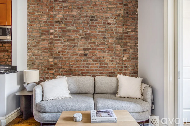 A grey couch with a white pillow is in front of a brick wall.
