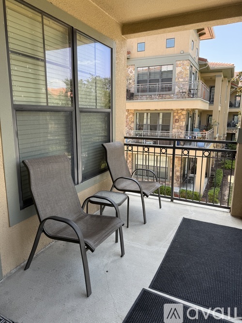 Two chairs are on a balcony with a view of a building.