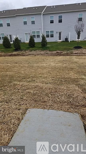 A grassy area in front of a grey building with a sign that says "bright MLS available".