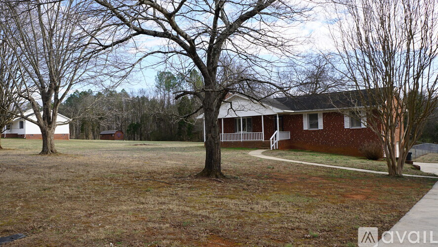 A house with a red brick exterior and a white porch is surrounded by trees and grass.