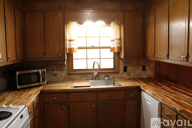 A kitchen with wooden cabinets and a window with curtains.