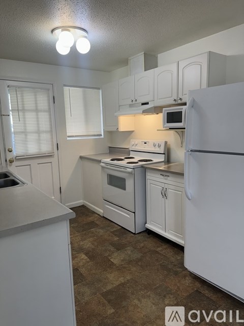 A kitchen with white appliances and brown flooring.