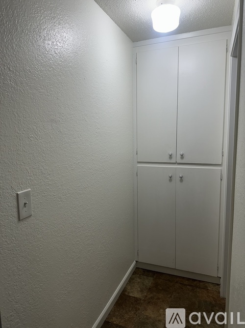 A white cabinet with two doors and two handles is in a room with a white wall and a light switch.