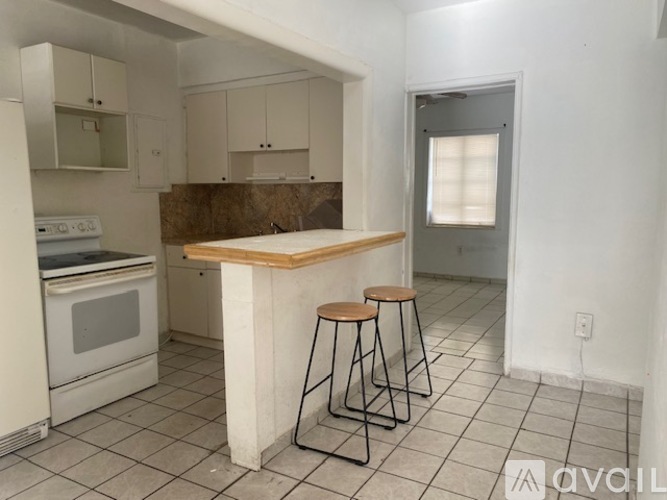 A kitchen with white appliances and a wooden island with two stools.