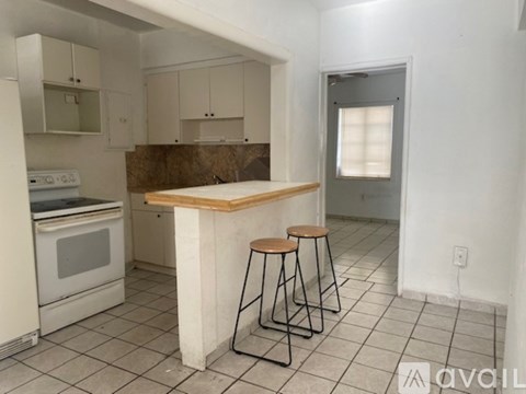 A kitchen with white appliances and a wooden island with two stools.