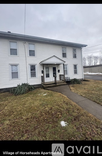 A white two-story apartment building with a porch and a sign that says "Village of Horseheads Apartments".