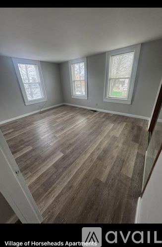 A room with wooden flooring and three windows at the Village of Horseheads Apartments.