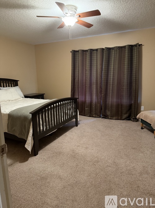 A bedroom with a bed, a fan, and a window with curtains.