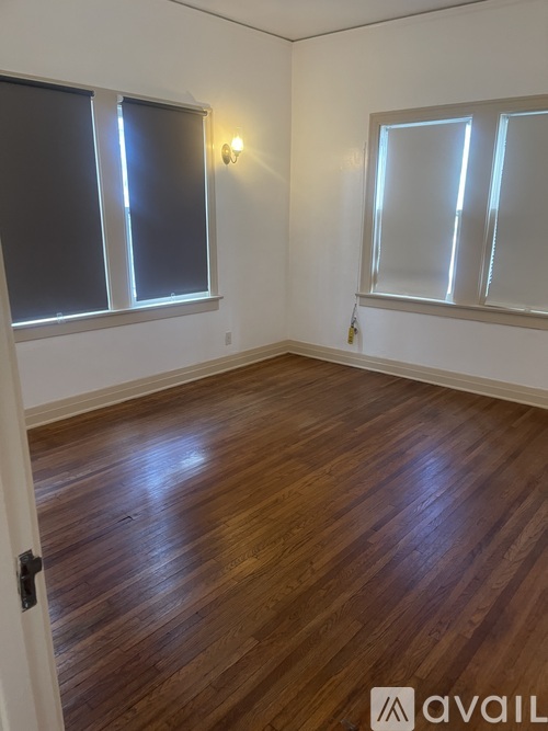 A room with wooden flooring and two windows.