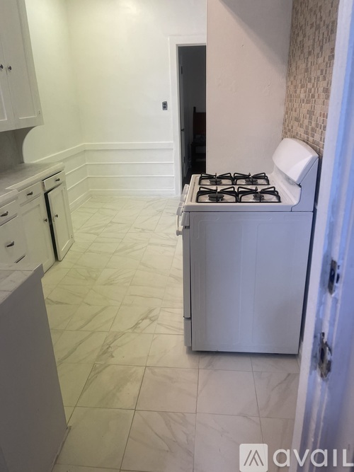 A white kitchen with a stove and a tiled floor.