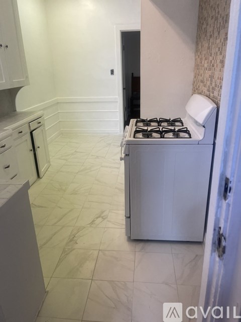 A white kitchen with a stove and a tiled floor.