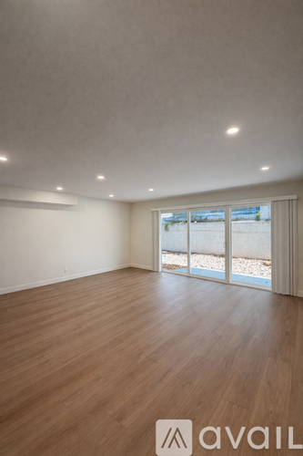 A room with wooden flooring and a window overlooking a gravel area.