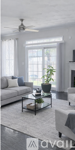 A living room with a white couch, a glass coffee table, and a ceiling fan.