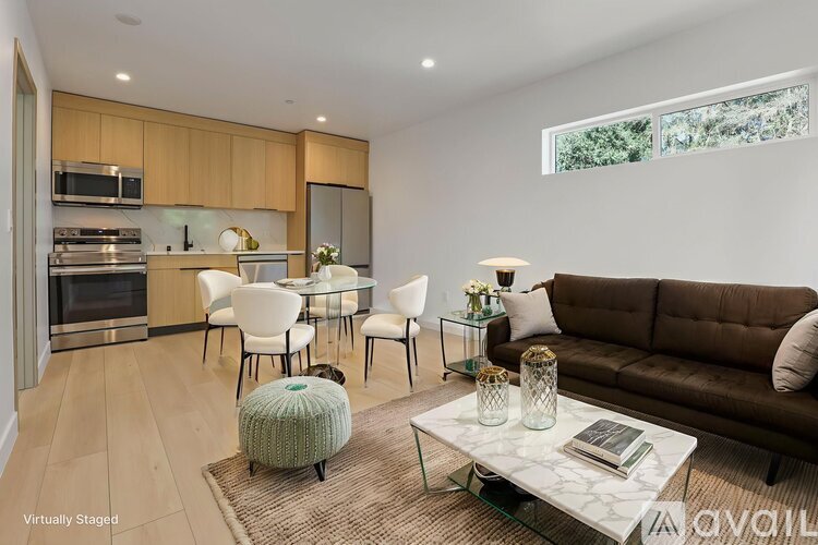A modern living room with a brown couch, a glass coffee table, and a kitchen area in the background.