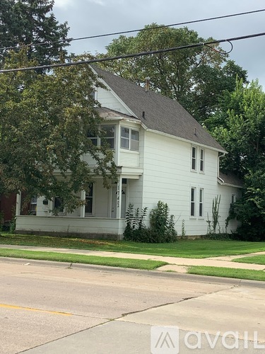 A white house with a porch and a tree in front.