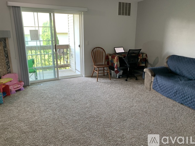 A living room with a blue couch, a chair, a small table with a laptop, and a window with a view of the outside.