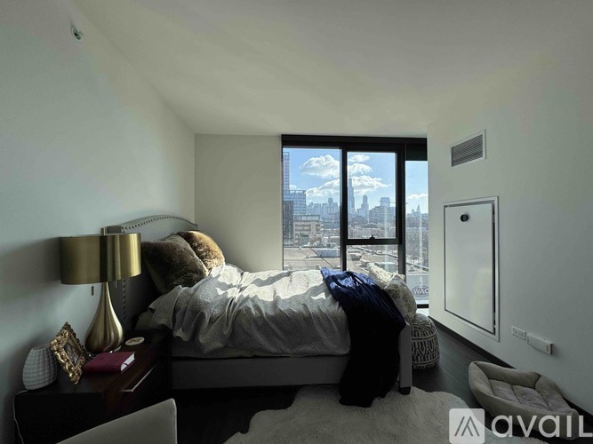A bedroom with a bed, a lamp, and a window overlooking a cityscape.