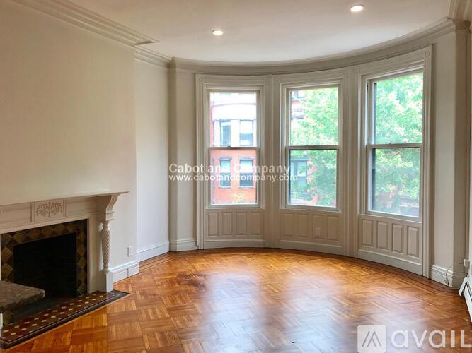 A large empty room with a fireplace and wood flooring.