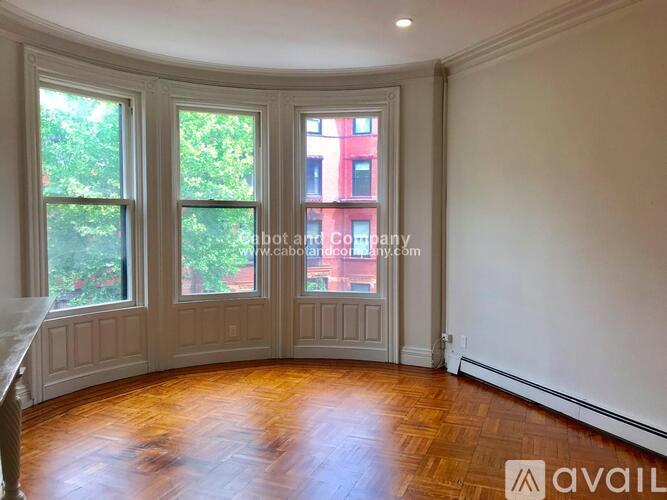 A room with wooden floors and a large window overlooking a red building.