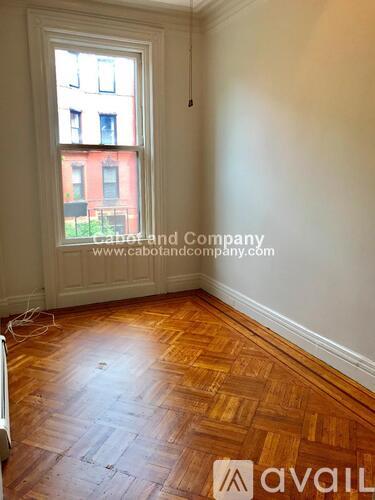 A room with wooden flooring and a window showing a red building outside.