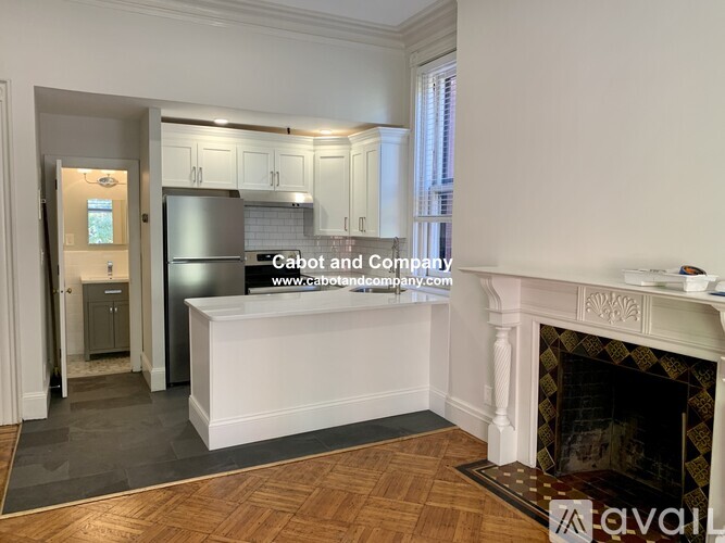 A kitchen with a refrigerator, cabinets, and a fireplace in a room with wooden flooring.
