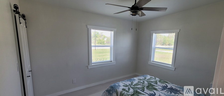 A bedroom with a bed, a ceiling fan, and two windows.