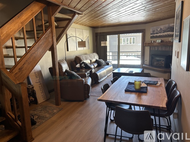 A living room with a wooden staircase and a dining table set with a black napkin and a yellow mug.