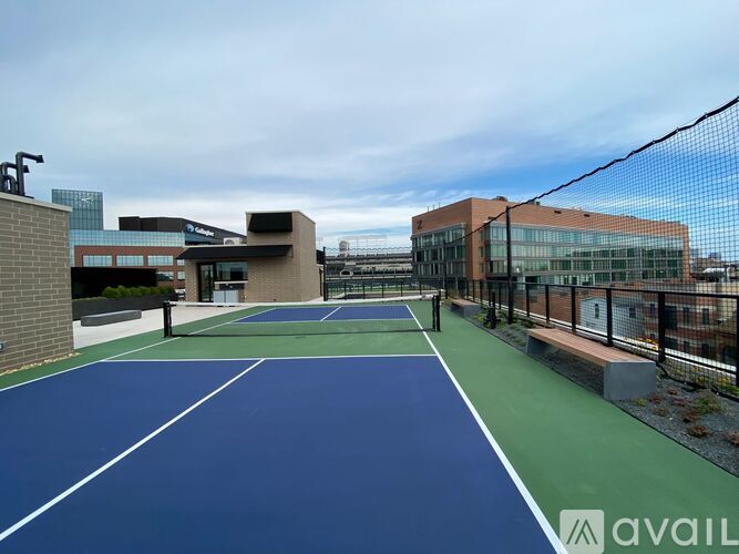 A tennis court with a blue surface and white lines is surrounded by a black fence.