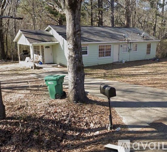 A green trash can sits next to a mailbox in front of a house.