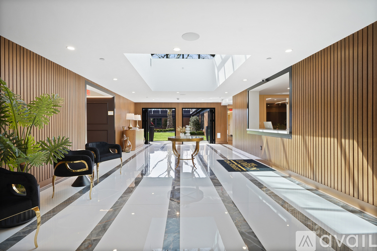 A long hallway with a marble floor and black chairs on the left side.